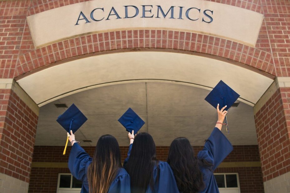 three girls in graduation gowns hold their caps in the air
